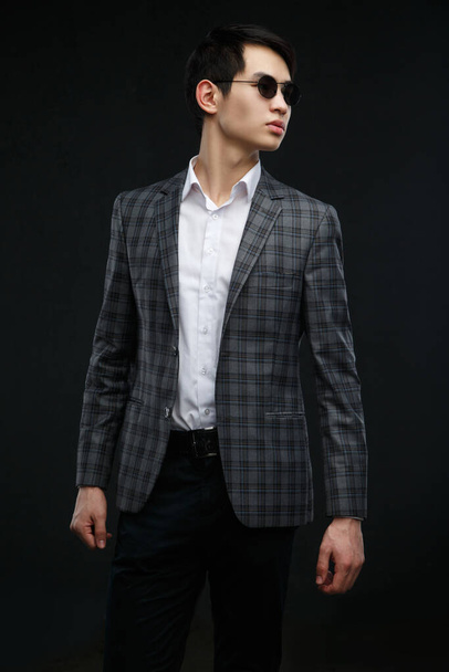 Young asian guy in a suit and sunglasses isolated on dark background. - Photo, Image