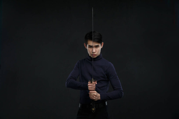 A young Asian man with a katana in his hands against a dark background. - Fotó, kép