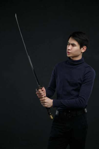 A young Asian man with a katana in his hands against a dark background. - Fotó, kép