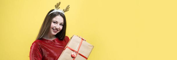 A girl in a red dress with gift against a yellow background. - Foto, imagen