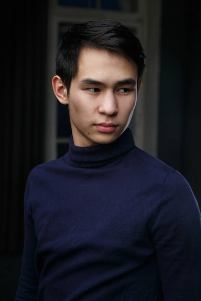 Portrait of a young Asian man in blue badlon in a dark room. - Фото, изображение