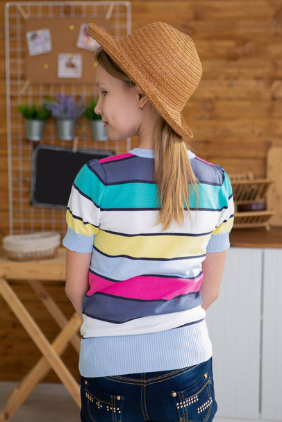 a girl in a straw hat is standing in the kitchen with her back to the camera - Фото, изображение