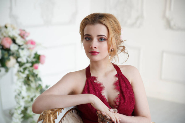 Porträt eines netten blonden Mädchens mit einer leicht eleganten Frisur in einem roten Kleid in einem hellen Raum. - Foto, Bild