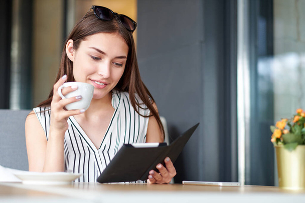 Young business woman in a cafe reading an ebook and drinking coffee - Photo, Image