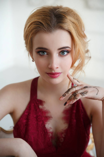 Portrait of a cute blonde girl with a light elegant hairstyle in a red dress in a bright room. - Foto, Imagen