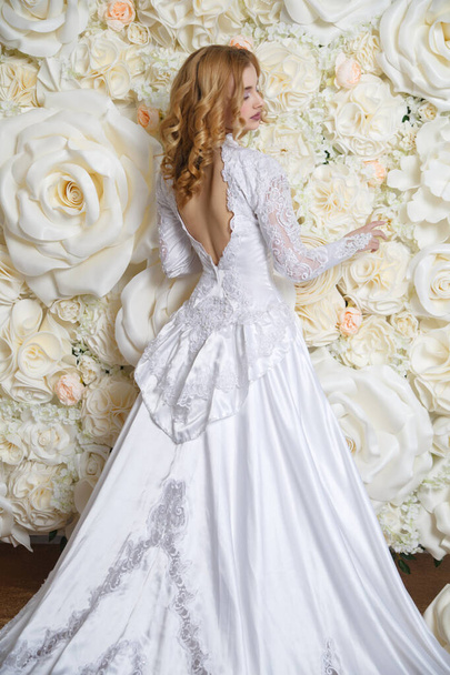 Elegant bride in a long vintage dress back view on the background of a photo zone of large white roses. - Fotoğraf, Görsel