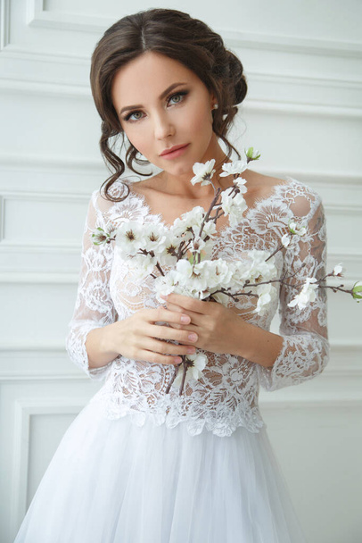 Portrait of a beautiful elegant bride with a bouquet of sakura in a bright interior. - Photo, Image