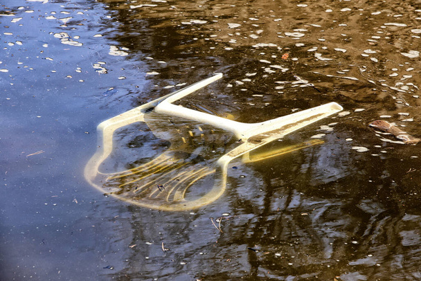 Παλιά βρώμικη λευκή πλαστική καρέκλα βυθισμένη στο νερό του ποταμού - Φωτογραφία, εικόνα