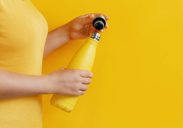 Nahaufnahme einer Frau, die eine gelbe Mehrwegflasche auf gelbem Hintergrund öffnet  - Foto, Bild