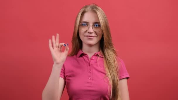 Šťastná mladá žena ukazuje ok znamení s prsty a mrkání izolované na červeném pozadí. - Záběry, video