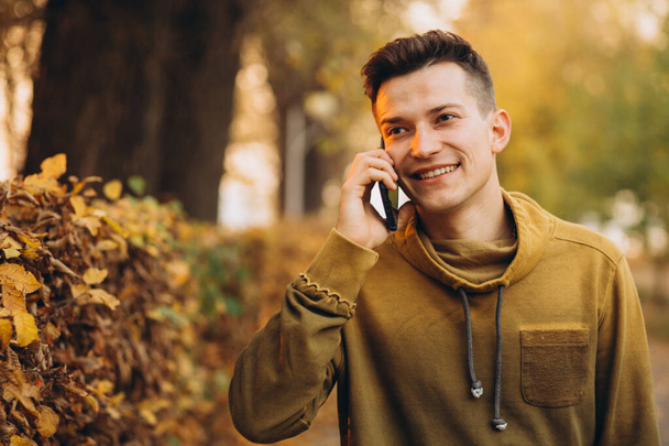 Retrato de chico guapo y feliz sonriendo y hablando por teléfono en el parque de otoño - Foto, imagen