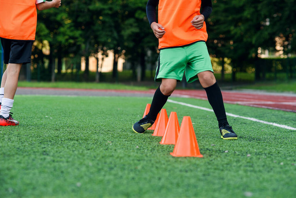 Chiudi le gambe dei giocatori di calcio in esecuzione tra coni di plastica arancione che in piedi sullo stadio artificiale durante l'allenamento. - Foto, immagini