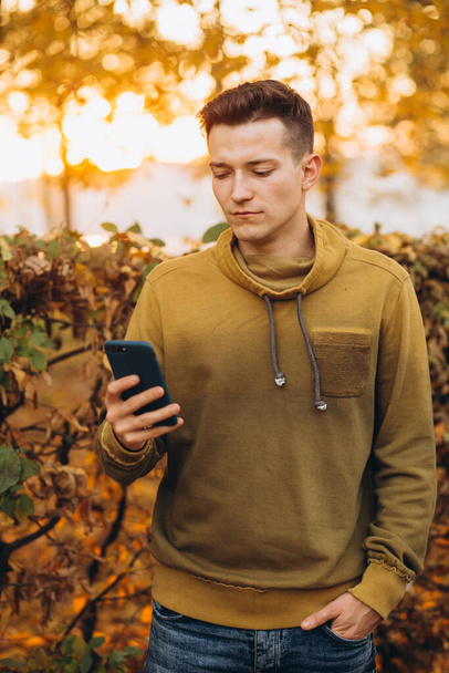Portret przystojnego i szczęśliwego faceta uśmiechającego się i rozmawiającego przez telefon w jesiennym parku - Zdjęcie, obraz