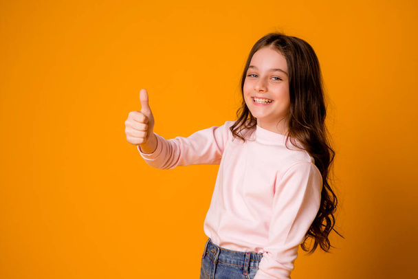 cute little girl in studio over orange background - Φωτογραφία, εικόνα