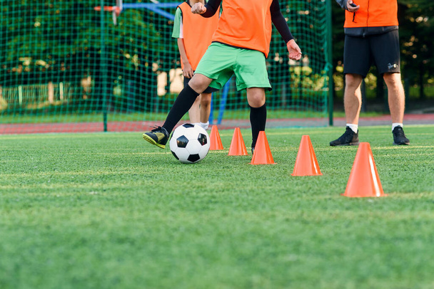 Close up teen boy in sportswear trains soccer at stadium and learns to circle the ball between training orange cones. - Foto, Imagen