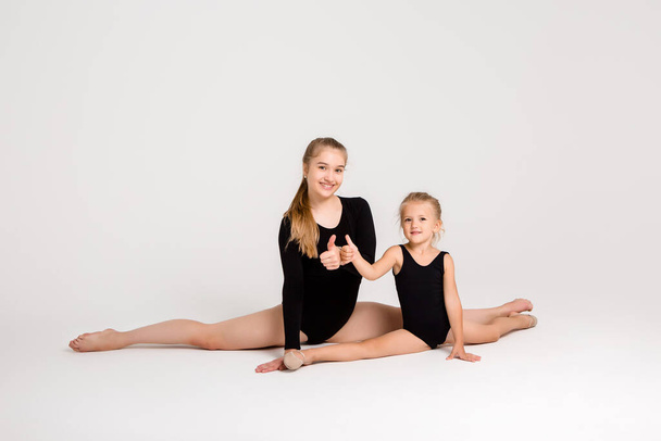 Genç kız jimnastik koçu ve küçük kız öğrenci beyaz arka planda baş parmak gösteriyorlar. - Fotoğraf, Görsel