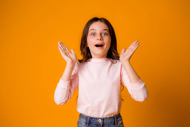 niedliches kleines Mädchen im Studio auf orangefarbenem Hintergrund - Foto, Bild