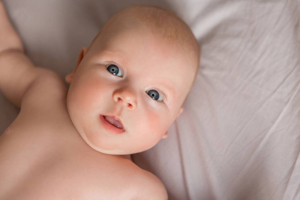 Ευτυχισμένο μωρό 3 μηνών που χαμογελάει, ξαπλωμένο στο λευκό κρεβάτι - Φωτογραφία, εικόνα