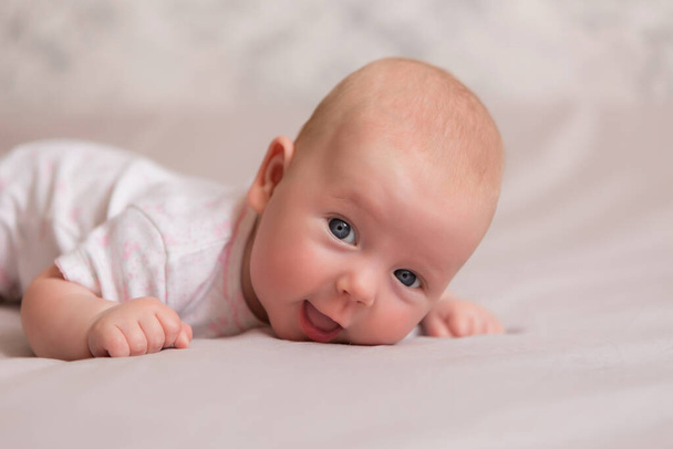 Saludable niña de 3 meses de edad en traje de cuerpo blanco se encuentra en la cama - Foto, Imagen
