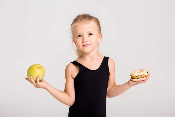 Tyttö hymyilee pitelee omenaa ja hampurilaista. Valitsemalla terveellistä ruokaa, ei pikaruokaa, tilaa tekstiä - Valokuva, kuva