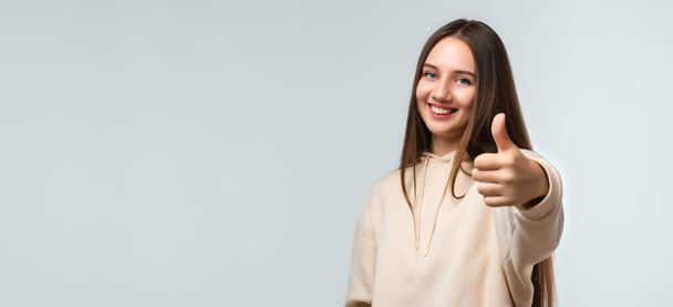 Happy Pretty young woman with long chestnut hair, Smiling and showing thumb up, dressed in casual clothes. I like that. Good job.Human emotions concept. Copy space for your text - Photo, Image