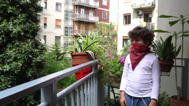Βαριέται αγόρι με μπαντάνα στο πρόσωπο ξοδεύοντας χρόνο στο μπαλκόνι κατά τη διάρκεια covid - Πλάνα, βίντεο