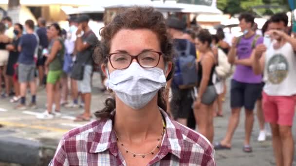 covid-19コロナウイルスのパンデミックの間に彼女の後ろの人々の群衆とマスクを持つ白い少女-社会的距離1メートル - 映像、動画