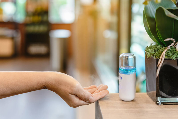 コーヒーショップでお客様にサービスを提供するコロナウイルス(Covid-19)の普及を防ぐために手洗浄用アルコールナノミストスプレー。現代の医療技術。新しい普通の生活様式。選択的焦点 - 写真・画像