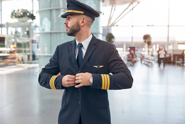 Schöner männlicher Pilot knöpft sich seine Jacke zu - Foto, Bild