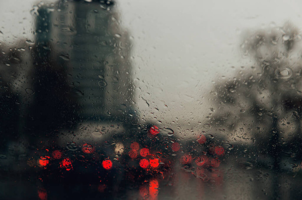 Şehir yolu, arabanın ön camına düşen yağmur damlalarının arasından görülüyor. Su damlalarına odaklan. - Fotoğraf, Görsel