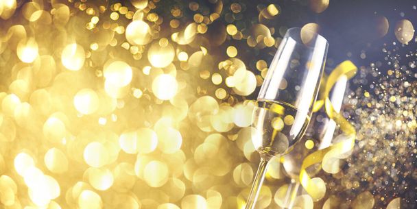 金色のリボンと金の輝きを持つ2つのシャンパングラスは、暗い背景にボケをスプラッシュ。豪華なレストランディナーのお祝い。クラシークリスマスと新年のパノラマデザインバナー. - 写真・画像