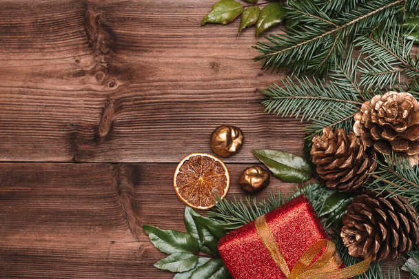 モミの木とマゴニアの枝、黄金のコーン、黄金の栗と暗い木製の素朴な背景に赤いギフトボックスで作られたクリスマスのフレーム。クリスマスの背景テキストのためのスペースをコピーし、トップビュー. - 写真・画像