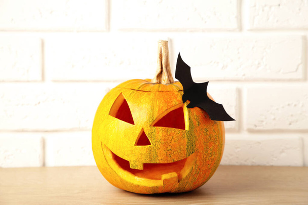 Carved glowing pumpkin and black bat on light background. Halloween celebration. Top view - Foto, Bild