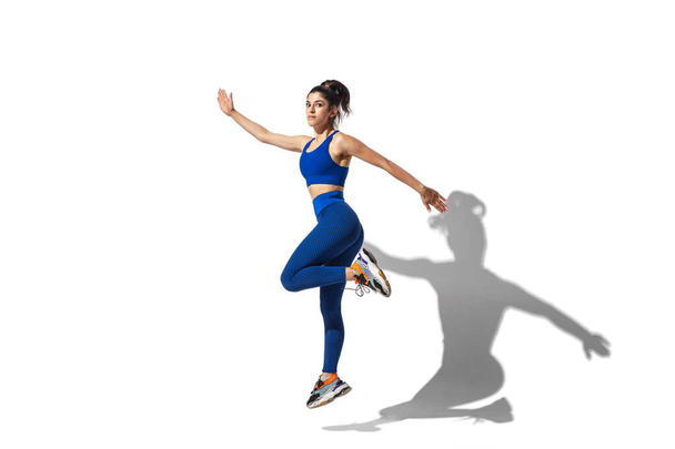 Beautiful young female athlete practicing on white studio background with shadows - Foto, Imagen
