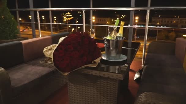 市街地のパノラマビューを望むレストランで2人用のテーブルを提供しています。レストランテラスでロマンチックなデート。背景に美しい夜の街のシーン。スローモーションドリーショット - 映像、動画