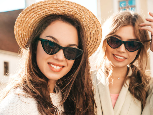 Two young beautiful smiling hipster female in trendy white sweater and coat. Sexy carefree women posing on street background in hat. Positive models having fun outdoors - Φωτογραφία, εικόνα