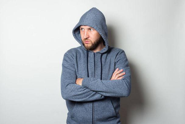 Young man in a hood with a serious, aggressive face looks to the side on a light background. - Фото, зображення