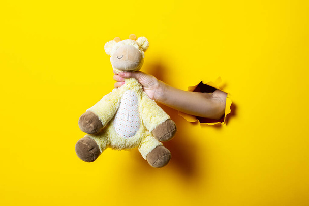 Το χέρι κρατά ένα παιδικό παιχνίδι σε κίτρινο φόντο. Χέρι γροθιές φόντο. - Φωτογραφία, εικόνα