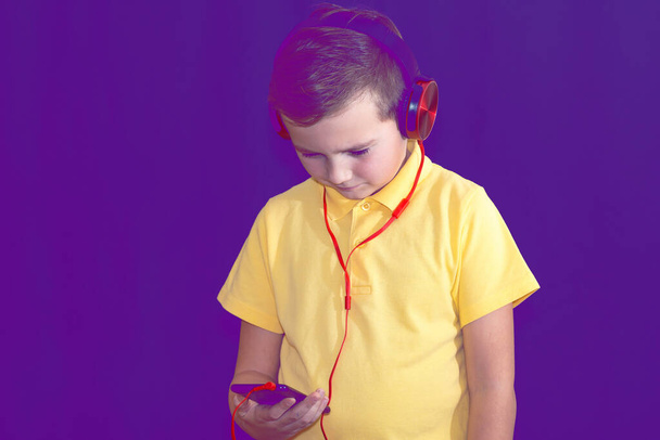 Close up of one young school boy using his phone and listening music alone or watching videos.Purple foggy toned background. - Photo, Image