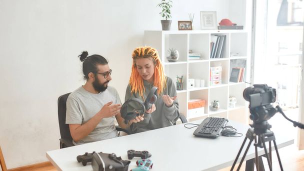 Man and woman holding, discussing headphones. Young male and female technology blogger recording video blog or vlog about new gadgets at home - Фото, зображення