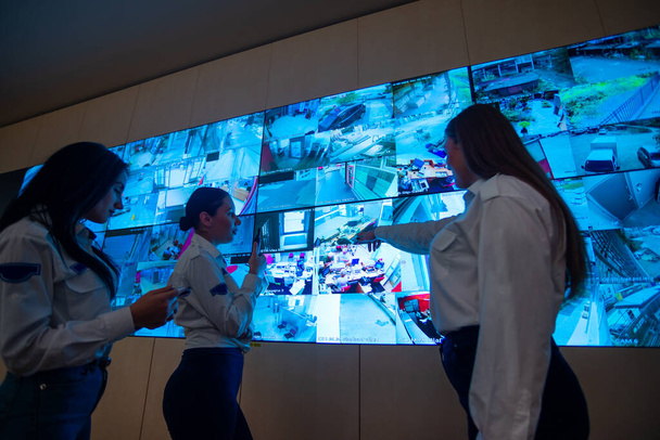 Guardie di sicurezza in piedi di fronte a un grande monitor CCTV presso la sala di controllo principale durante la lettura e la discussione di piani - Foto, immagini