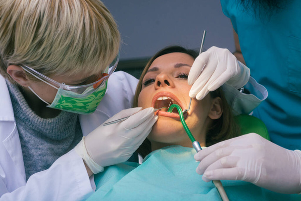 Профессиональные стоматологи мужского и женского пола осматривают женские зубы в стоматологическом кабинете - Фото, изображение