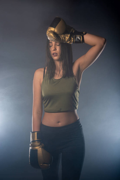 Smokey portrait of an attractive fit girl wearing boxing gloves posing with her arm over her head. - Foto, Imagen