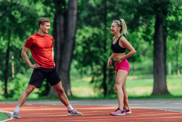 Young couple stretching before starting their morning jogging routine on a tartan track at the park. - Fotoğraf, Görsel