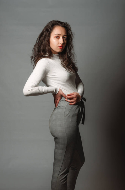 Portrait d'un beau modèle féminin posant en pull blanc sur un mur gris - Photo, image