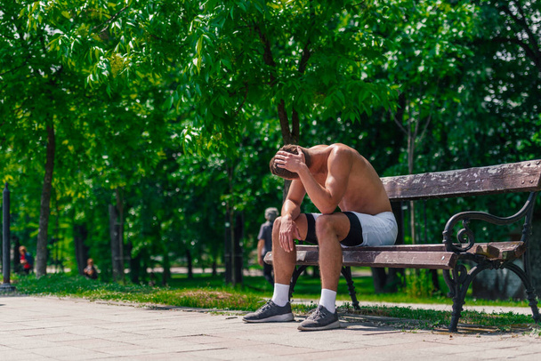 Κουρασμένος όμορφος αθλητής ξεκουράζεται στον πάγκο στο πάρκο μετά το τρέξιμο - Φωτογραφία, εικόνα