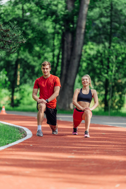 Young couple stretching before starting their morning jogging routine on a tartan track at the park. - Fotoğraf, Görsel
