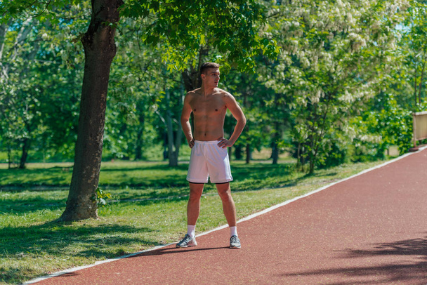 Young athlete without t-shirt is standing on a running track in the park - Zdjęcie, obraz