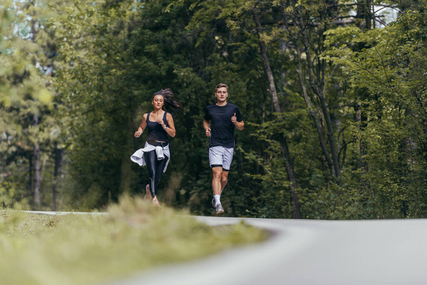 Jovem casal apto atheltes correndo na estrada em uma floresta. - Foto, Imagem