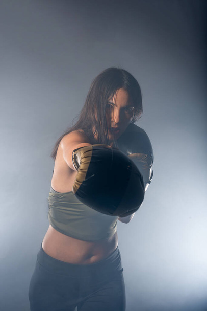 Foggy image of a young and sexy female boxer punching direct hit with boxing gloves - Photo, Image